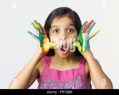 Jeune fille AVEC DES COULEURS SUR LE VISAGE ET LES MAINS APRÈS AVOIR JOUÉ AU FESTIVAL DE HOLI EN INDE. Tourné SUR UN FOND UNI Banque D'Images