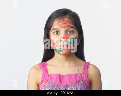 Jeune fille AVEC DES COULEURS SUR LE VISAGE ET LES MAINS APRÈS AVOIR JOUÉ AU FESTIVAL DE HOLI EN INDE. Tourné SUR UN FOND UNI Banque D'Images