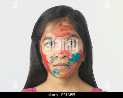 Jeune fille AVEC DES COULEURS SUR LE VISAGE ET LES MAINS APRÈS AVOIR JOUÉ AU FESTIVAL DE HOLI EN INDE. Tourné SUR UN FOND UNI Banque D'Images