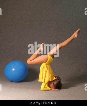 Une fille dans une robe jaune dans la salle de sport s'est engagé dans la gymnastique, une boule bleue se trouve à côté d'elle. Banque D'Images