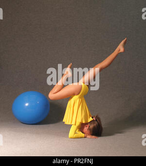 Une fille dans une robe jaune dans la salle de sport s'est engagé dans la gymnastique, une boule bleue se trouve à côté d'elle. Banque D'Images