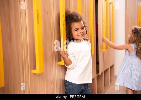 Heureux les enfants multiculturels debout près des casiers dans la maternelle vestiaire Banque D'Images