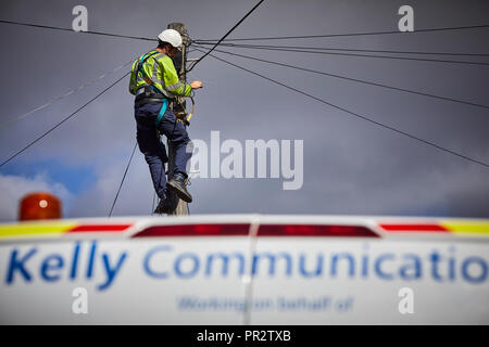 Telecome entrepreneurs Ingénieur de Kelly Communications escalade un poteau téléphonique pour fixer une ligne téléphonique sous-traitant travaillant pour BT Openreach en ma Banque D'Images