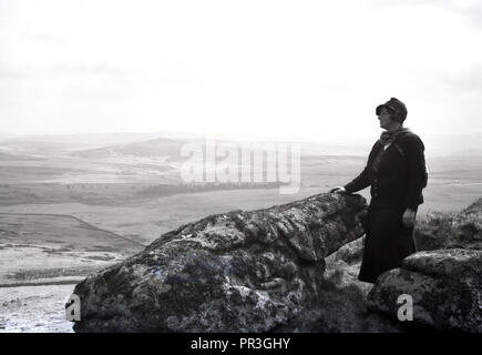 Années 1930, historiques, une femme assise sur un pic rocheux ou Tor à l'ensemble au cours de la parc national de Dartmoor dans le Devon, England, UK, un paysage naturel sauvage qui contient de nombreux affleurements de granit Connu comme cadre de référence. Banque D'Images