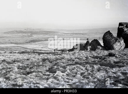 Années 1930, historiques, femme assise sur un pic rocheux ou Tor au parc national de Dartmoor dans le Devon, England, UK, un landes sauvages qui contient de nombreuses formations rocheuses naturelles ou des affleurements de granit Connu comme cadre de référence. Banque D'Images