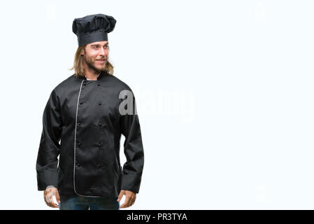 Beau jeune homme aux cheveux longs cook sur fond isolé smiling à côté et regardant loin de penser. Banque D'Images