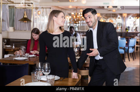 Beau gentilhomme barbu aider les jeunes femme séduisante avec sa chaise dans restaurant Banque D'Images