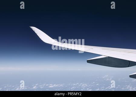 Aile de vol d'un avion moderne plus de nuages contre ciel bleu foncé. Banque D'Images