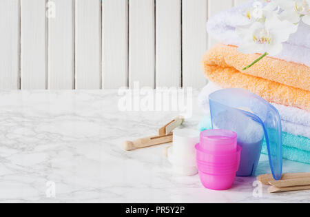 Récipient de mesure en plastique bleu avec du produit de lavage, les contenants avec du détergent, pile de serviettes blanches et pinces à linge en bois, fleur d'orchidée blanche Banque D'Images