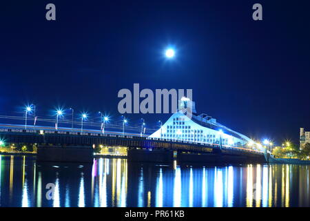 Riga, Lettonie - Sep 20, 2018 : La Bibliothèque nationale de Lettonie également connu sous le nom de Gaismas Pils (Château de la lumière) et pont de pierre sur la Daugava à lumière de lune. Banque D'Images