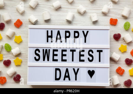 Conseil moderne avec texte 'Happy Sweetest Day' mot et candy over white background, vue de dessus. À partir de ci-dessus, mise à plat, vue du dessus. Banque D'Images