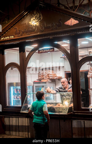 Damas / Syrie - 25/07/2018 : photo de nuit d'un gosse d'acheter un croissant croissant de shop dans une étroite ruelle de la vieille ville, près de la mosquée des Omeyyades. Banque D'Images