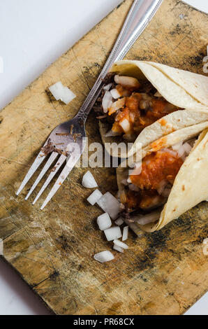 Tacos au boeuf avec oignons et sauce rouge, servi sur une planche de bois brûlé, fourche sale avec de la viande et les oignons autour. Banque D'Images