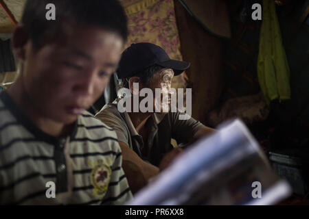 Un homme vu regarder la TV à l'intérieur de sa maison pendant que son petit-fils, passer du temps sur son téléphone mobile près de la ville de Tsogt-Ovoo à Ömnögovi Province dans le sud de la Mongolie. Banque D'Images