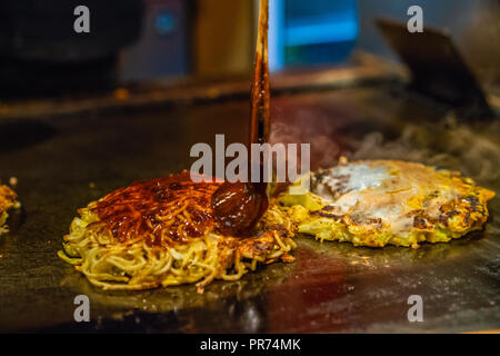 Chef, c'est la cuisson des aliments traditionnels japonais qui s'appelle Okonomiyaki, elle est l'ajout de sauce épicée dans l'aliment Banque D'Images