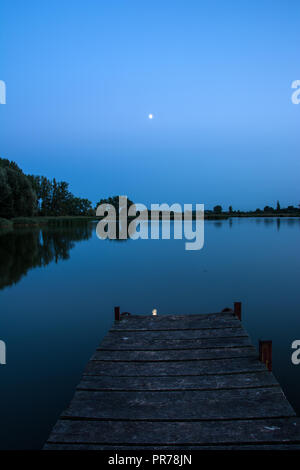 Pont de bois sur un lac calme et la lune dans le ciel du soir Banque D'Images