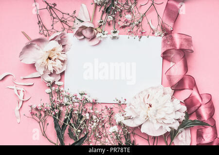 Arrangement de fleurs et pétales autour de papier blanc sur fond rose avec des rubans, vue du dessus. L'amour sentiment lettre. Style Instagram. Invitation de mariage. Banque D'Images