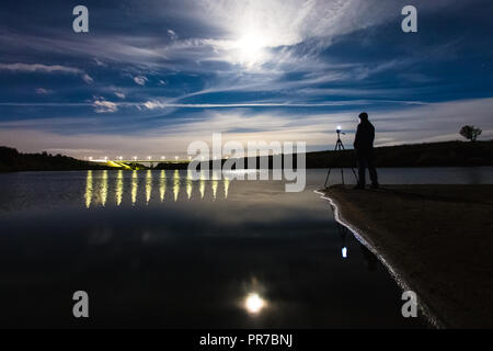 L'aide photographe professionnel comme smartphone appareil photo sur trépied pour capturer le paysage de nuit avec la pleine lune, ciel nuageux et la rivière Banque D'Images