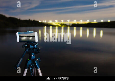 En utilisant comme smartphone appareil photo professionnel sur trépied pour la capture de nuit paysage avec beaucoup de lumière reflétée sur surface de l'eau Banque D'Images