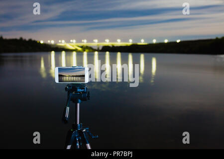 En utilisant comme smartphone appareil photo professionnel sur trépied pour la capture de nuit paysage avec beaucoup de lumière reflétée sur surface de l'eau Banque D'Images