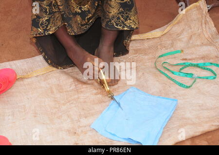 Buyende, Ouganda. Septembre 29th, 2018. Scovia Nambi, 42 ans, résident d'Butaaswa Buyende village en coupe de district un tissu avec une paire de ciseaux à l'aide de ses pieds après avoir assisté à son jardin de manioc. Elle ne s'adaptant que sa petite entreprise. Elle a prouvé que le handicap n'est pas l'incapacité. C'était avant les célébrations de son 42e anniversaire avec le ministre du Tourisme à la Martinique Royaume Hellen Namutamba (pas en photo) qui avait rendu visite. Nambi, mère de deux enfants, n'a pas les deux bras mais prouve au monde entier qu'elle peut laver ses vêtements, faire de la couture, la cuisine et s'occuper de son Banque D'Images