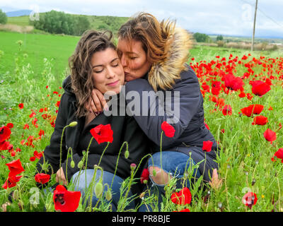 L'Espagnol mother kissing her daugther jeunes adultes heureux et bénéficiant d'un champ de fleurs de pavot en automne en Espagne Banque D'Images