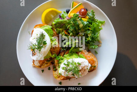 Oeufs Royale, oeufs pochés au saumon fumé gravlax () et d'avocat avec un mélange de salade de fruits frais and​ sur une plaque blanche Banque D'Images