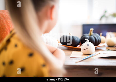 Jeune fille assise à une table, la décoration de citrouilles Halloween little white. Au cours de l'épaule. Bricolage d'Halloween et de l'arrière-plan de vie. Banque D'Images