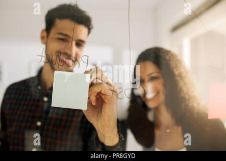 Business couple écrit le post-it collé sur le mur de verre transparent dans le bureau. Collègues de bureau d'affaires de discuter des idées et des plans sur une transpa Banque D'Images