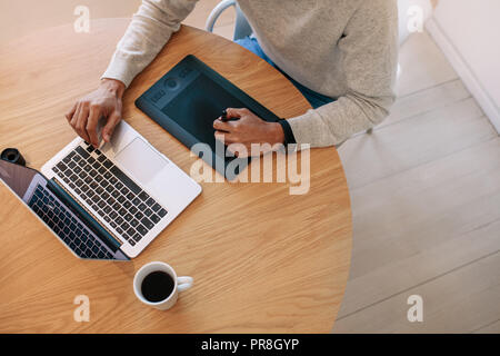 Vue de dessus a un pavé numérique connecté à un ordinateur portable assis sur une table. L'homme écrit sur un pavé d'écriture électronique en utilisant digi Banque D'Images