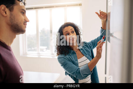 Femme entrepreneur de discuter affaires des idées et des plans sur une carte dans le bureau. Portrait sur un tableau blanc et d'expliquer alors que son collègue Banque D'Images