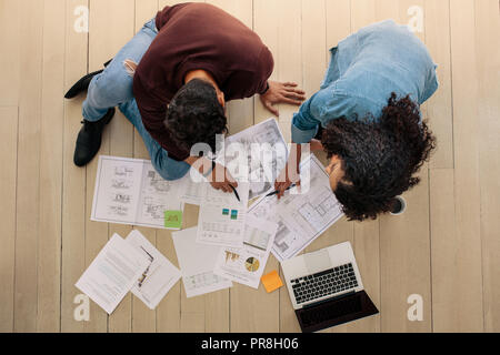 Vue de dessus de partenaires d'affaires assis sur le plancher et en discutant avec les documents d'affaires et un coffre à l'avant. Business man and woman discussing work Banque D'Images