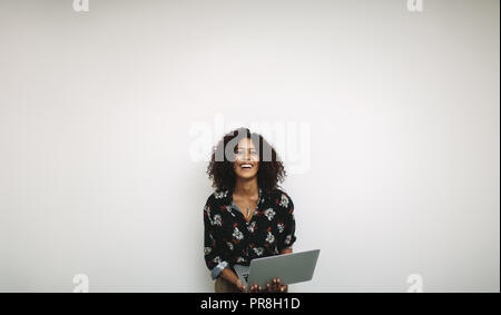 Femme entrepreneur détenant un ordinateur portable debout sur un fond blanc et de rire. Portrait of a businesswoman standing avec un ordinateur portable. Banque D'Images