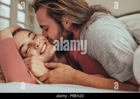 Couple in bed de passer du temps ensemble avec l'homme s'embrasser son partenaire. Femme souriante avec les yeux fermés d'être embrassé et aimé par son homme. Banque D'Images
