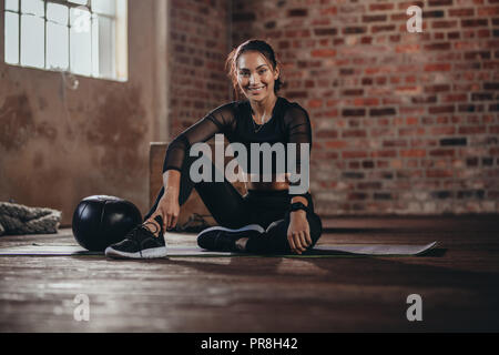 Portrait d'une jeune femme lors d'une pause dans la salle de sport. Hispanic female sitting on floor looking at camera, se reposant après l'entraînement. Banque D'Images