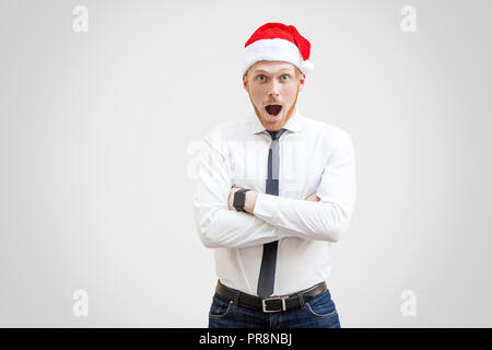 Portrait de demandé handsome businessman en chemise blanche, cravate noire et rouge nouvelle année hat, looking at camera avec étonnement le visage et mains croisées à l'intérieur. Banque D'Images
