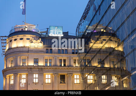 Un hôtel reflète dans la vitre d'un immeuble moderne comme la nuit tombe en place Vörösmarty, Budapest Banque D'Images