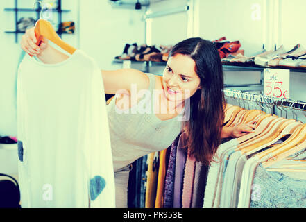 Jeune femme en choisissant Nouveau chemisier à manches longues vêtements en boutique Banque D'Images