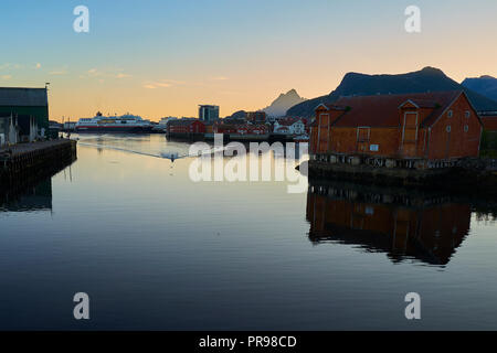 Coucher de soleil sur vieux entrepôts norvégienne de la pêche au bord de l'eau dans le port de Svolvær, le Ferry Hurtigruten MS TROLLFJORD, dans le centre. Iles Lofoten. Banque D'Images