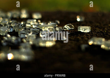 Les éclats de verre qui reflètent la lumière du soleil sur le sol sombre. Banque D'Images