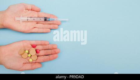 Les mains tenant les comprimés de médicaments différents et un autre avait holding syringe, le choix des médicaments avec fond bleu. Banque D'Images