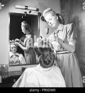 Obtenir une coiffure de 1940s. Une jeune femme aux cheveux foncés se regarde dans le miroir du salon de coiffure pour femmes tandis qu'un coiffeur met en forme et façonne les cheveux en 1940s cheveux typiques. Suède 1947. Photo Kristoffersson réf. AB22-7 Banque D'Images