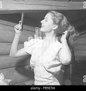 Femme fixant ses cheveux dans les 1940s. Une jeune femme blonde se regarde dans un miroir de poche tout en peignant ses cheveux. Suède 1945. Photo Kristoffersson réf. P146-4 Banque D'Images