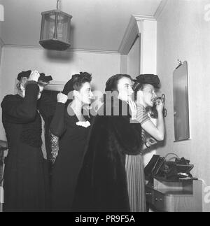 Les femmes se prépare pour une soirée dans les années 40. Le groupe de quatre femmes font la touche finale à leurs cheveux, les vêtements et le maquillage. Ils essaient tous de se faire une idée d'eux-mêmes dans le petit miroir sur le mur. Suède 1944. Kristoffersson Photo ref M93-6 Banque D'Images