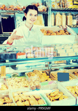 Jeune vendeuse positive posant avec cookies au compteur dans sweets shop Banque D'Images