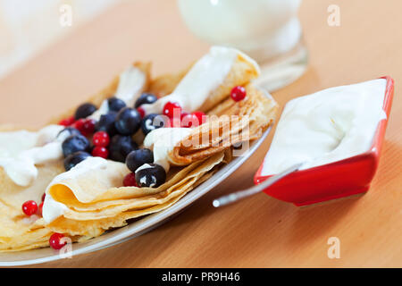 Gros plan du délicieux petit-déjeuner. Sweet pancakes aux fruits rouges sur la plaque blanche et crème laitière à table prêt à manger Banque D'Images