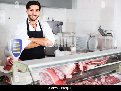 Souriant heureux boucher positive est debout sur son lieu de travail dans le marché. Banque D'Images