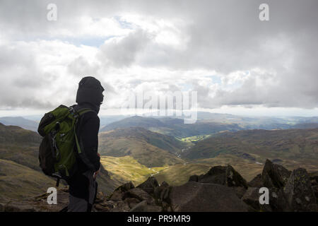 Un hillwalker profitant de la vue depuis le sommet du Bowfell à vers Hard Knott sur un coudy jour dans le Lake District, Cumbria, Angleterre. Banque D'Images