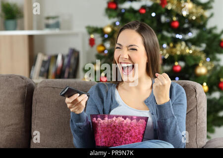 Excited woman watching tv sur Noël assis sur un canapé dans la salle de séjour à la maison Banque D'Images