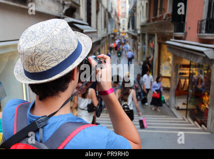 Garçon avec chapeau prend de nombreuses photos d'une rue étroite appelée Calle en langue italienne à Venise en Italie Banque D'Images